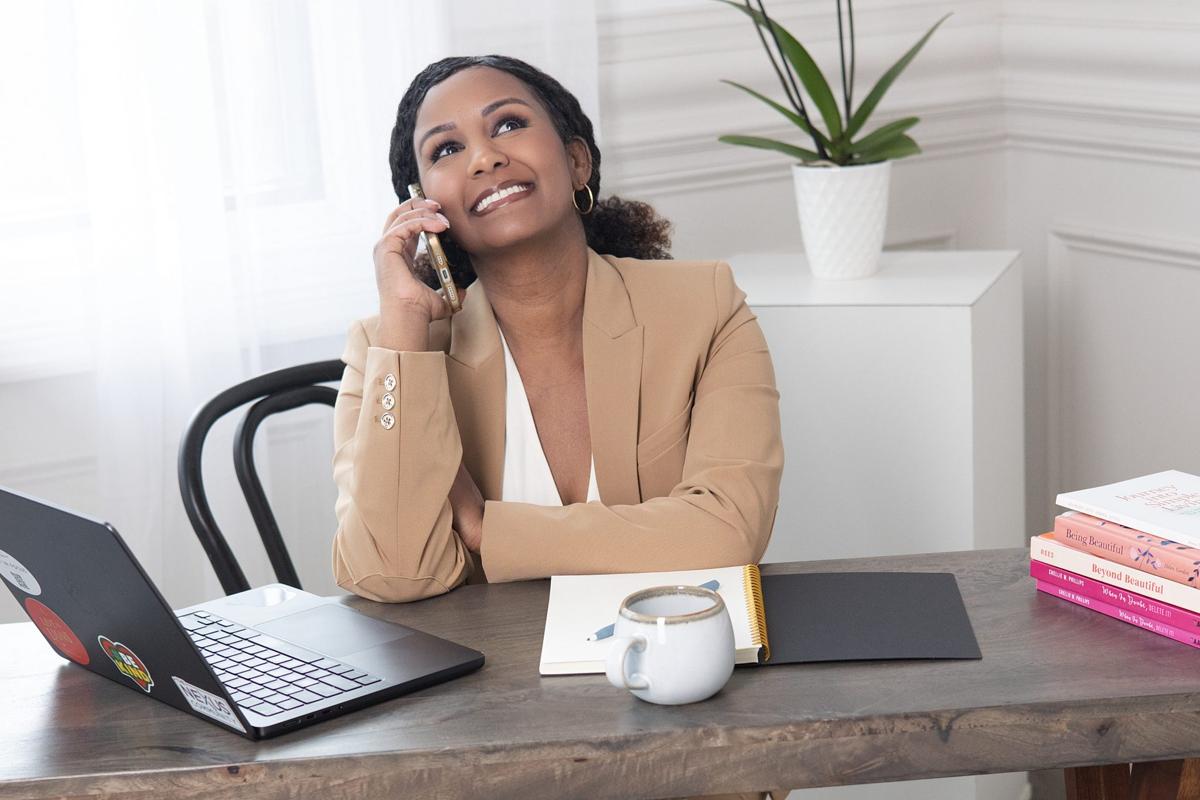 Brand photo of an entrepreneur in a camel blazer laughing on a phone call at her desk