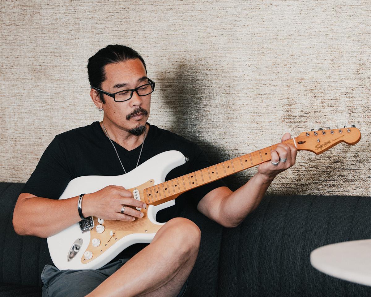 Personal branding portrait of a musician in glasses playing a white electric guitar on a sofa