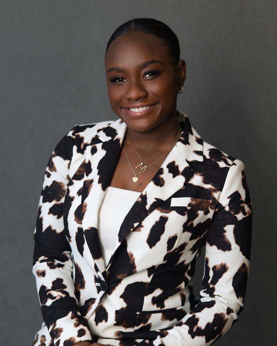 Studio headshot of a smiling woman in a black-and-white print blazer against a grey backdrop