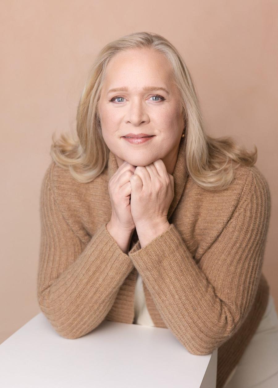 Warm studio portrait of a woman in a camel sweater with her hands clasped