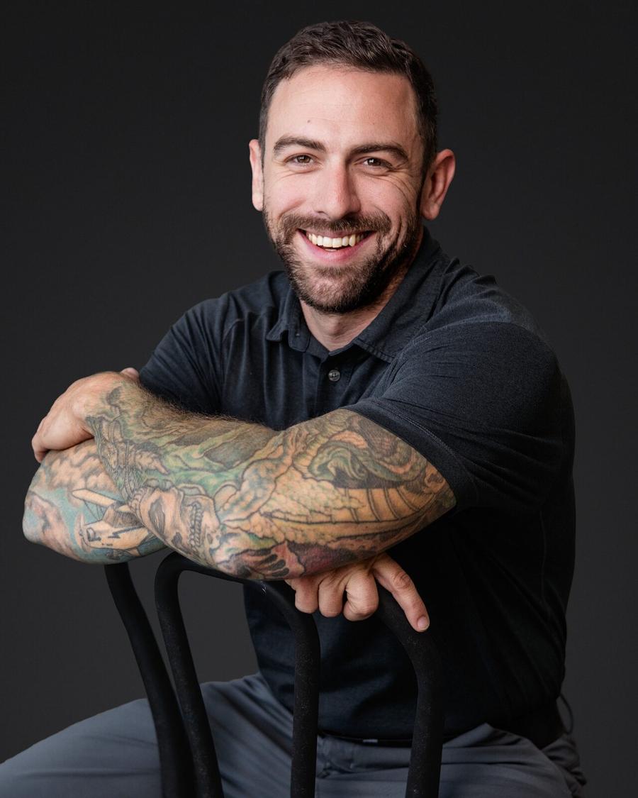 Personal brand headshot of a smiling man in a black polo seated on a stool