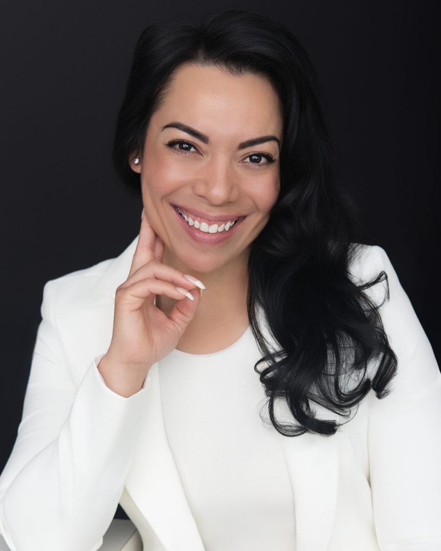 Professional headshot of a smiling woman in a white blazer against a black backdrop
