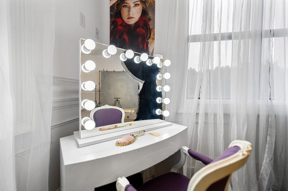 Lighted vanity mirror and a purple upholstered chair by the window