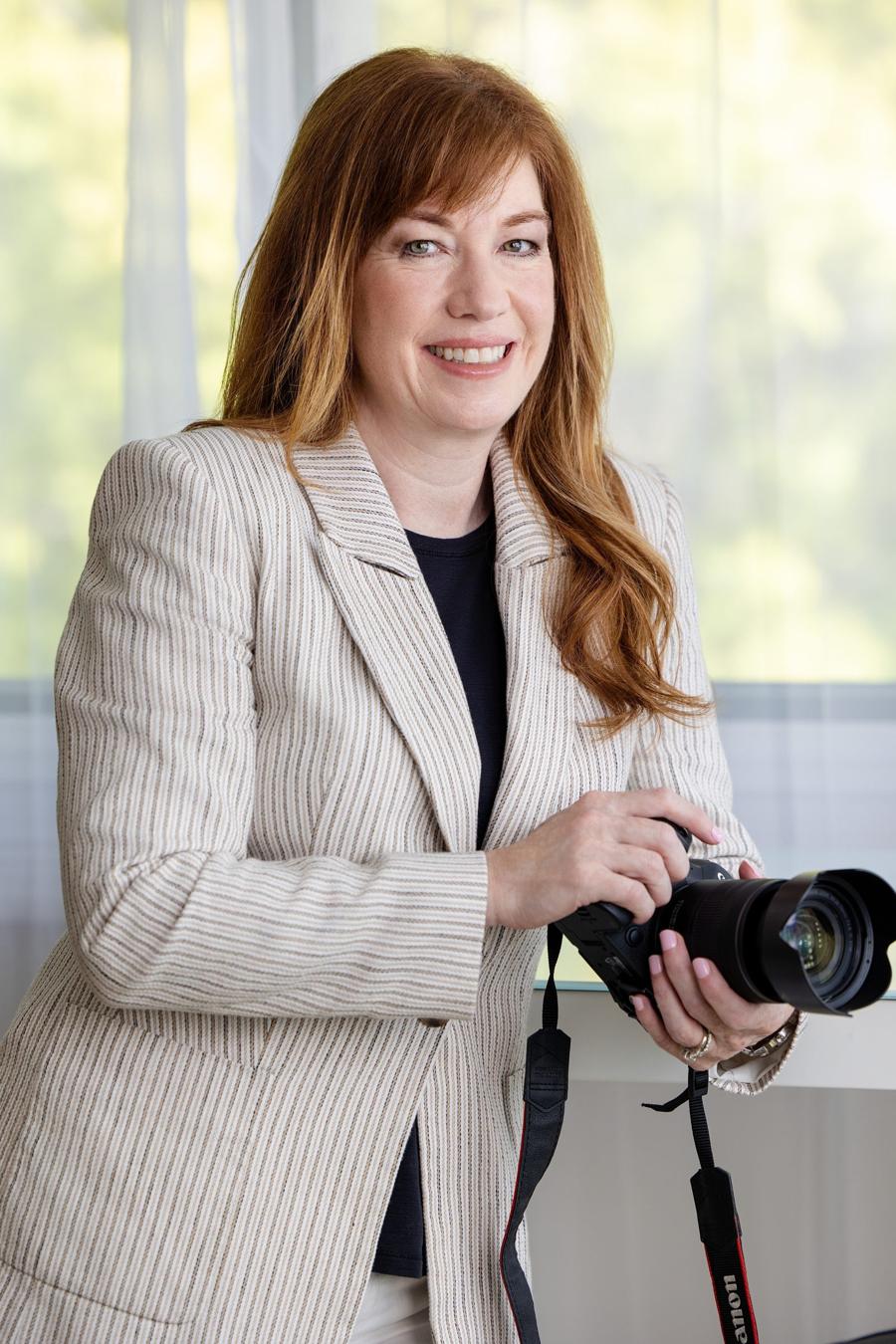 Personal branding portrait of a photographer in a striped blazer smiling with her camera