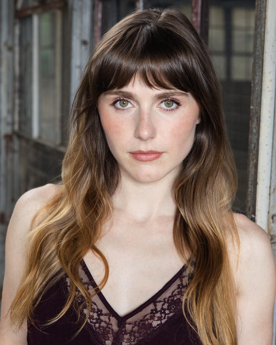 Actor headshot of a young woman with long brown hair and bangs in an industrial loft