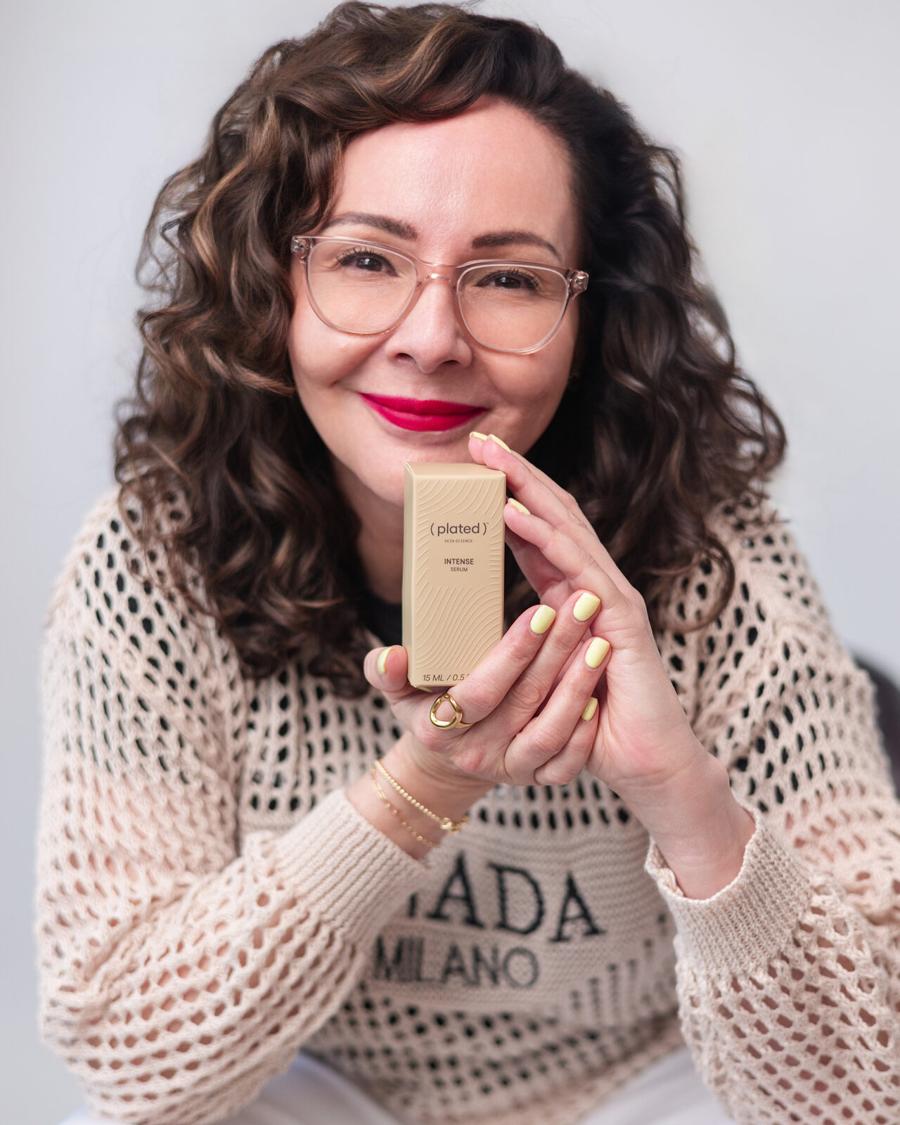 Personal brand headshot of a woman with curly hair and glasses holding her skincare product