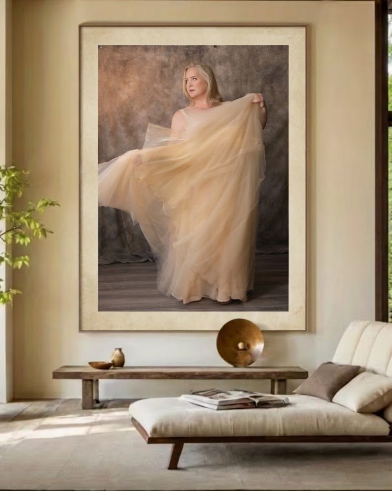 Large framed portrait of a woman in a flowing gold gown hanging above a bench in a sunlit living room